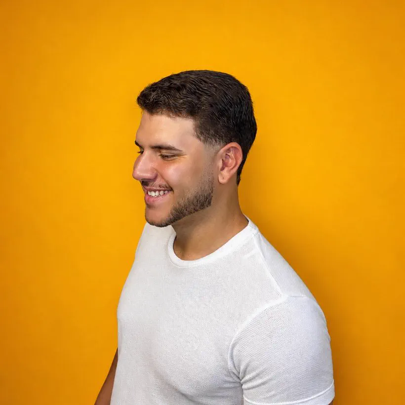 Cliente da Barbearia 08 sorrindo após o corte, em fundo amarelo